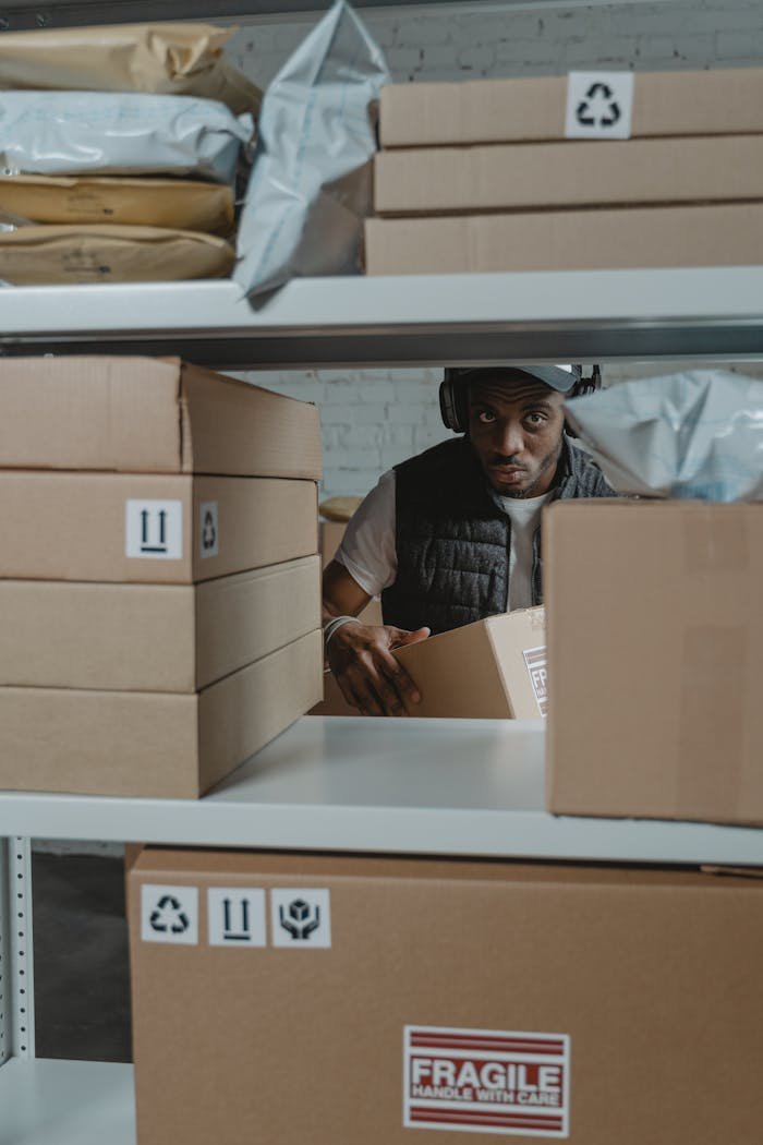 services-03 Man organizing packages on shelves in a warehouse setting with cardboard boxes.